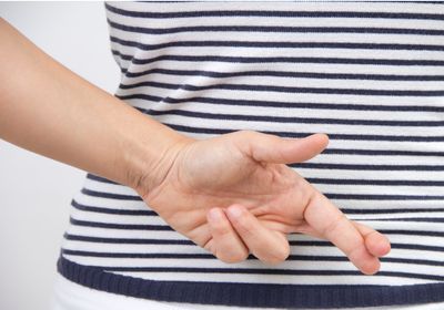 A woman in a blue and white striped shirt crosses her fingers behind her back.