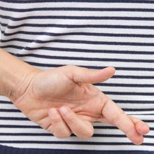 A woman in a blue and white striped shirt crosses her fingers behind her back.