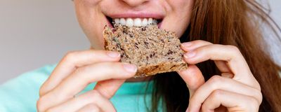 A woman eating a piece of multigrain bread.