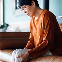 Middle aged woman sitting on a sofa, holding her knee in pain.