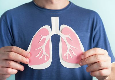 A man in a blue shirt holds a pinkish paper cut out of a pair of lungs.