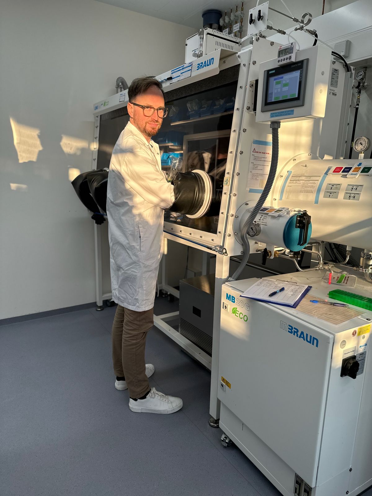 A man wears a laboratory coat. His hands are inside a safety laboratory hood.