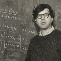 black and white photo of Richard Lewontin standing in front of a chalkboard covered in equations