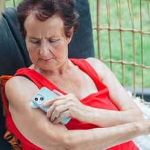 A woman with diabetes checks her blood glucose levels using a wearable biosensor patch on her upper arm, transmitting the results to a smartphone.