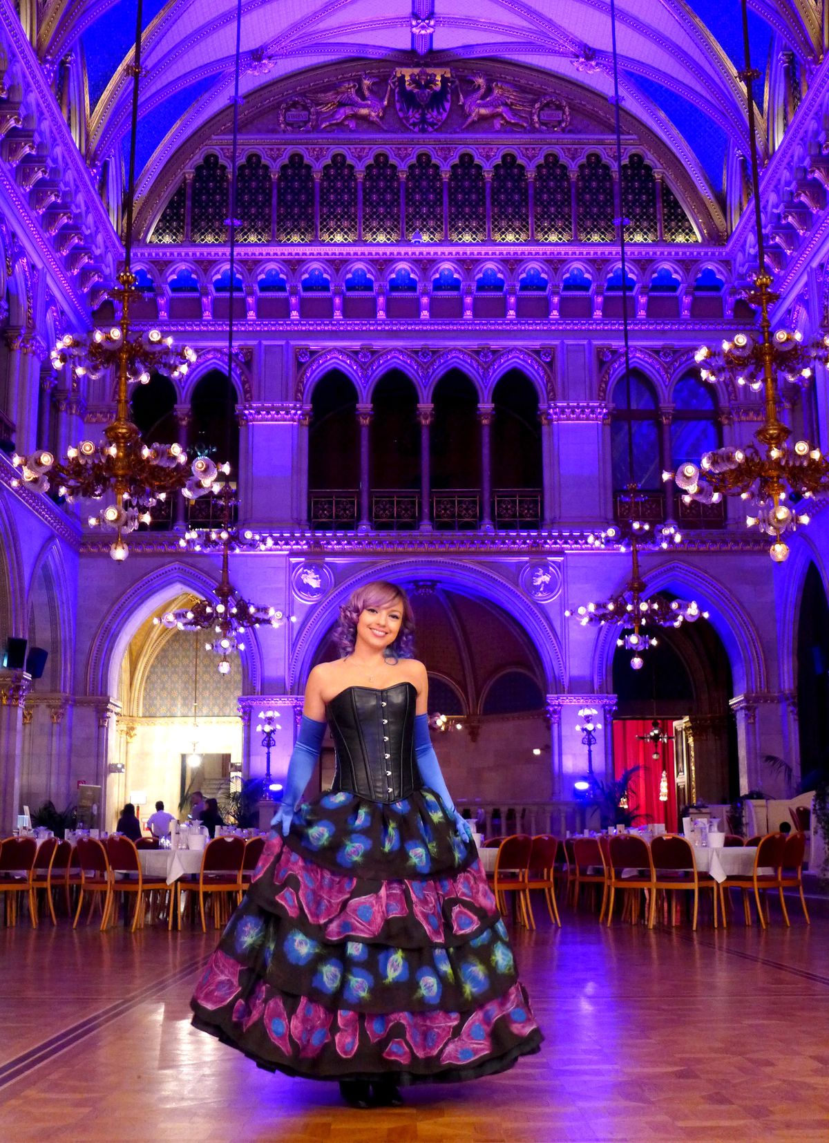 Beata Mierzwa stands in a ballroom wearing a dress for a fashion show. Her skirt contains images of fluorescently-labeled cells that she imaged on a microscope and printed onto the fabric.