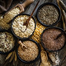 A top-down view of bowls filled various high-fiber foods such as rice, corn, seeds, and cereal sitting on a wooden table.