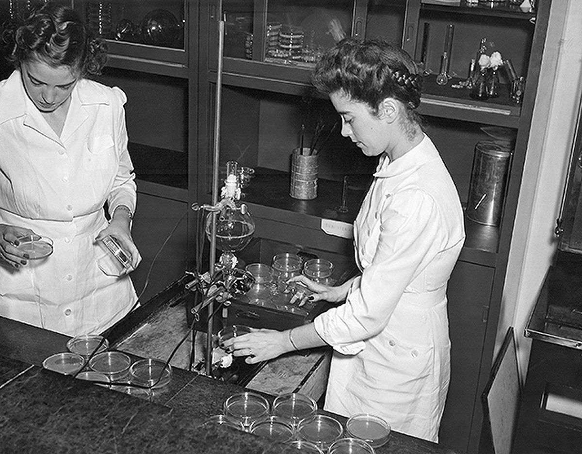 A black and white image of two women in white lab coats working with culture plates.