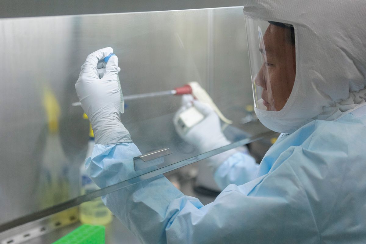 A researcher wears gloves and pipettes liquid in a fume hood.