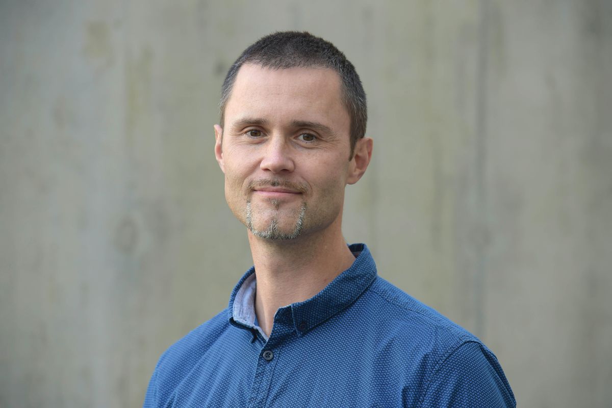 Michael Hiller wears a blue shirt and stands outside against a grey wall.