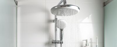 Image of a showerhead with running water. There is a soap dispenser and toothbrush on a wire shelf in the shower.