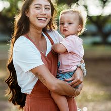 A smiling woman holds a young child outside in the park.