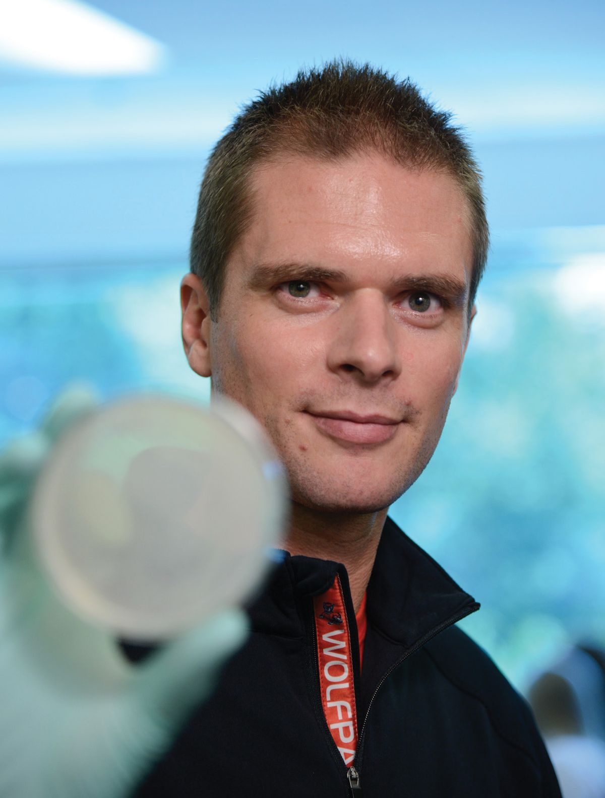 A man wears a black jacket and looks at the camera. He is holding a culture dish with his hand.