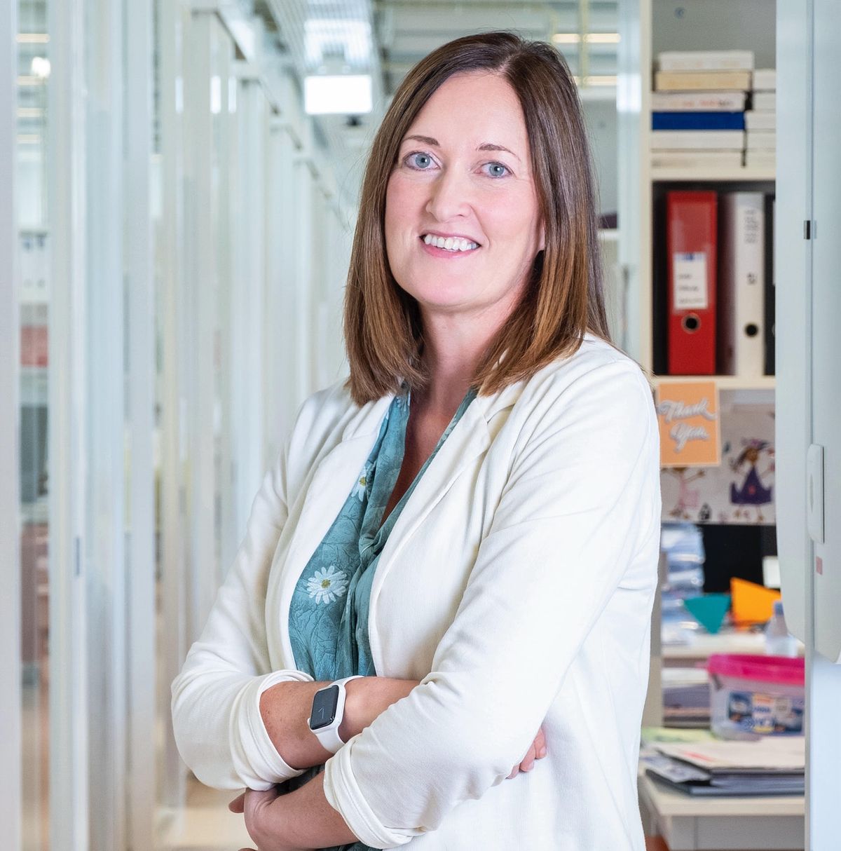 Johanna Joyce has shoulder-length brown hair and is wearing a white blazer over a blue shirt. 