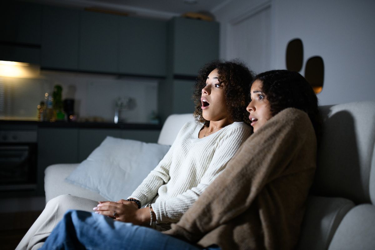 Two women enjoy a late-night horror movie, captivated by the suspense and thrill of the cinematic experience.