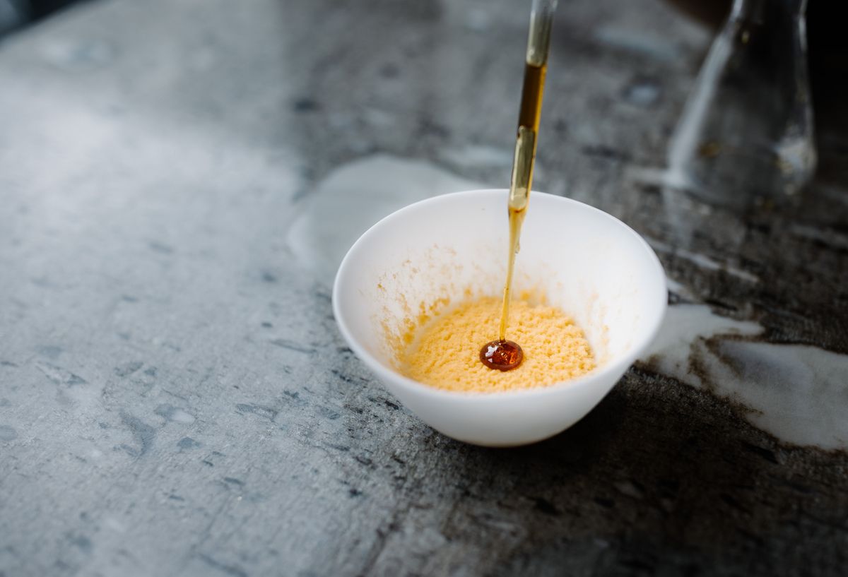 Photo of an orange rice custard in a white bowl with an eye dropper releasing a sweet brown syrup to the dessert.