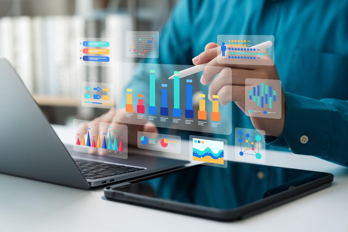 An individual using a laptop and tablet to create and analyze data-based graphics.