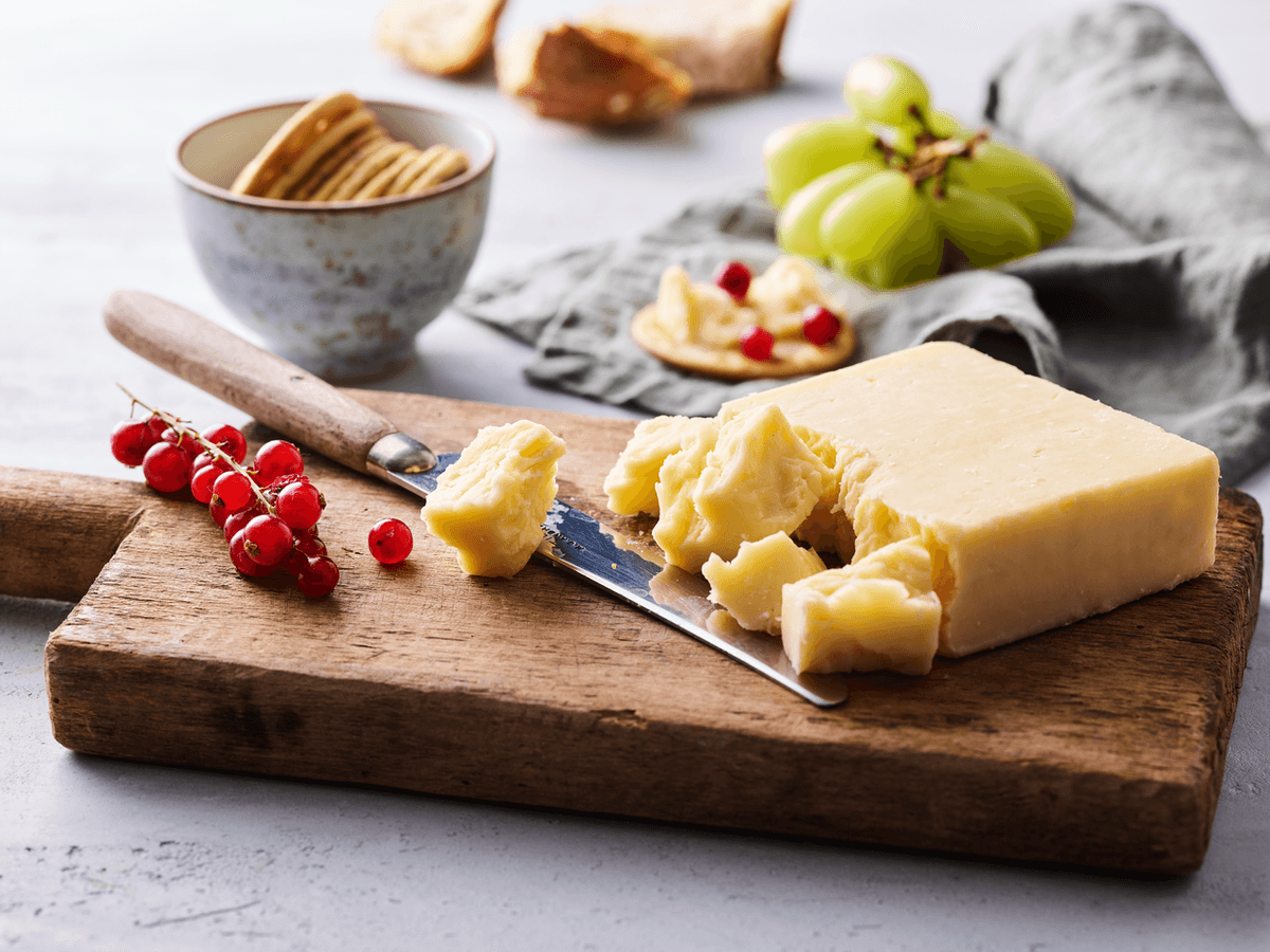 A block of cheddar cheese is pictured with various accompaniments. 