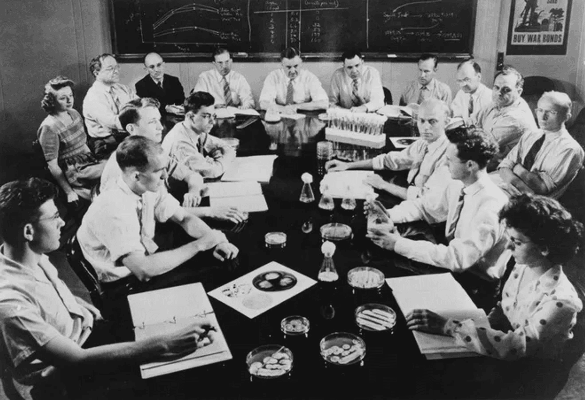 A black and white image of several researchers sitting around a table.