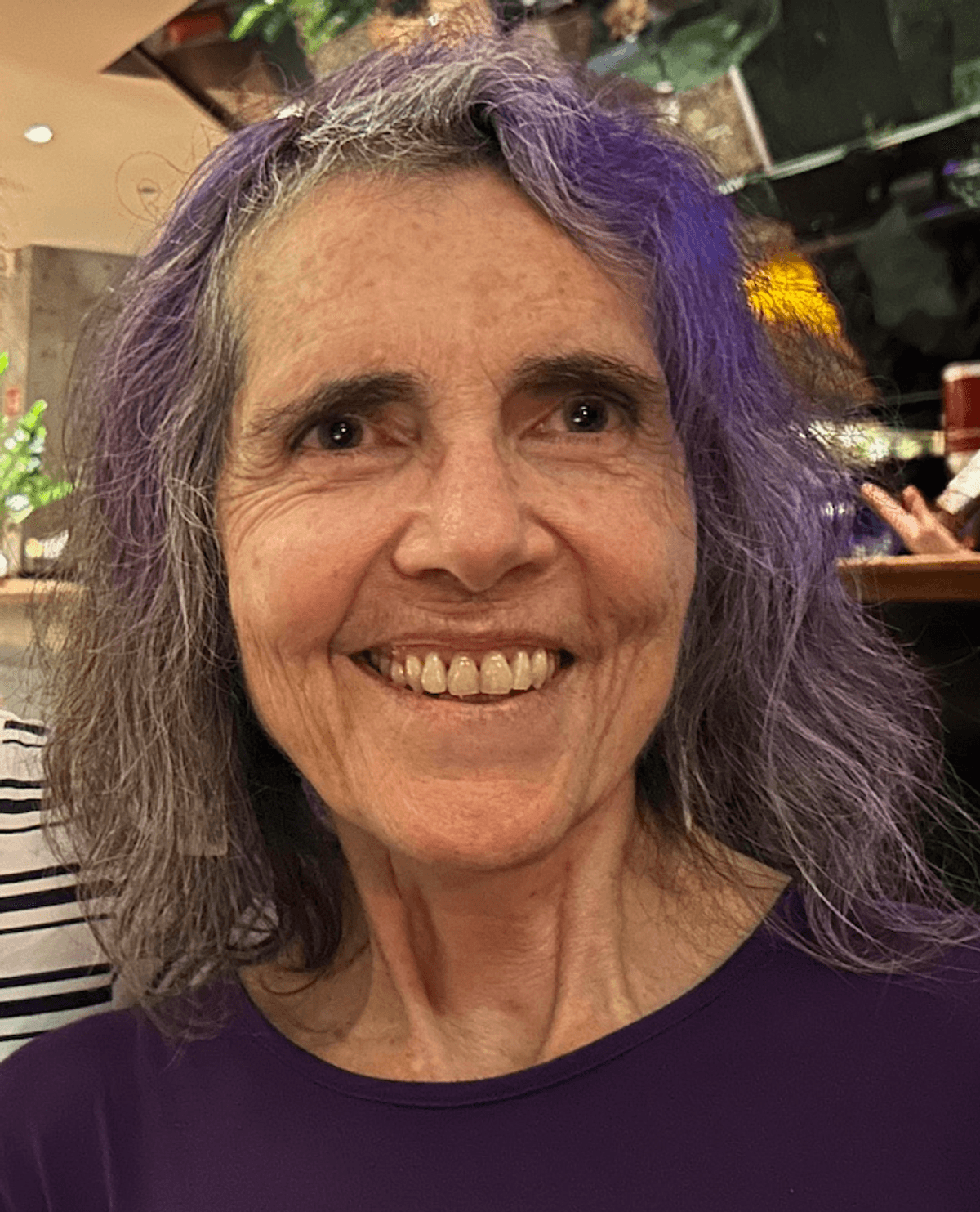 Nancy Keller wears a purple shirt and smiles at the camera.